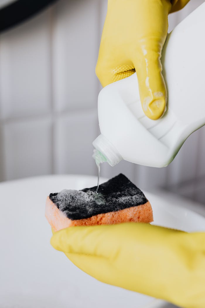 services-02 Crop faceless person in yellow latex protective gloves pouring cleaning agent from bottle to sponge in bathroom