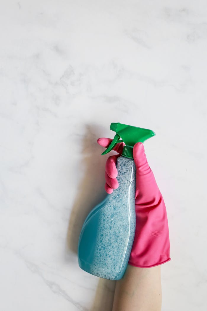services-03 Close-up image of a hand in a pink glove holding a spray bottle against a white background.