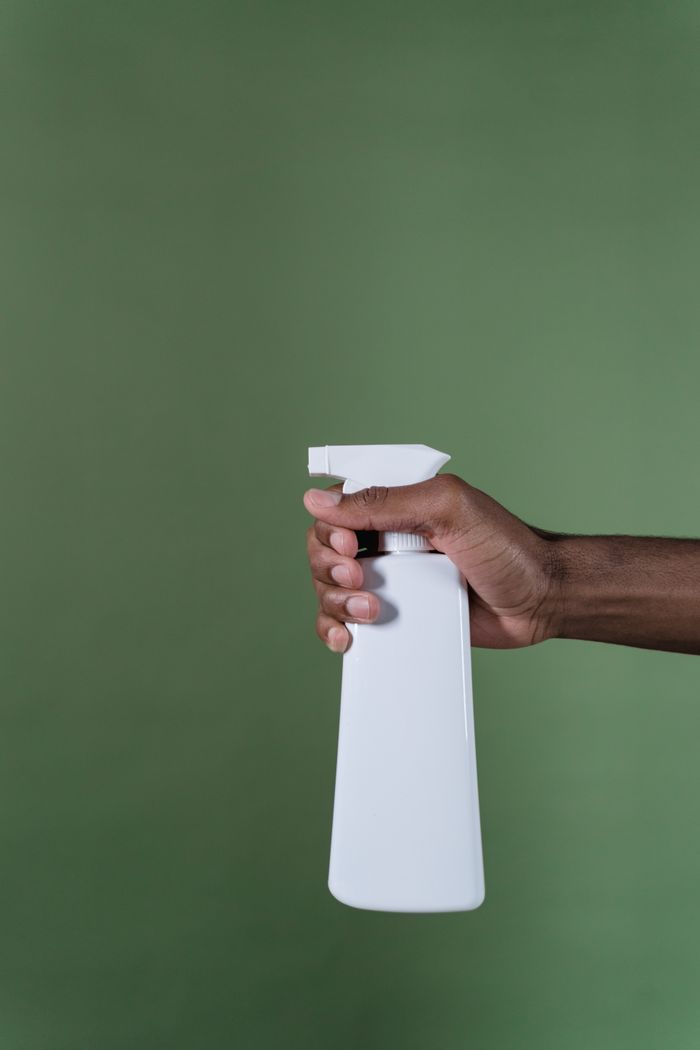 services-04 A close-up image of a hand holding a white spray bottle against a plain green background.